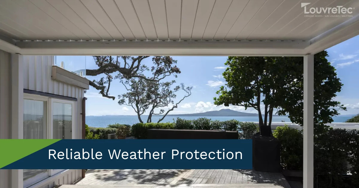 Outdoor patio with a white Louvretec opening roof overlooking the ocean and trees.