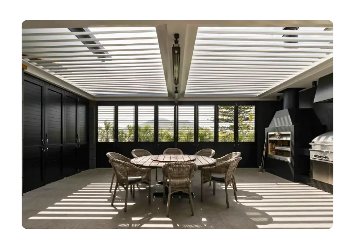 Stylish outdoor dining area with a round table, wicker chairs, and a louvered roof system.