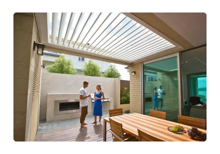 Couple enjoying an outdoor alfresco area with a louvered pergola and built-in barbecue.
